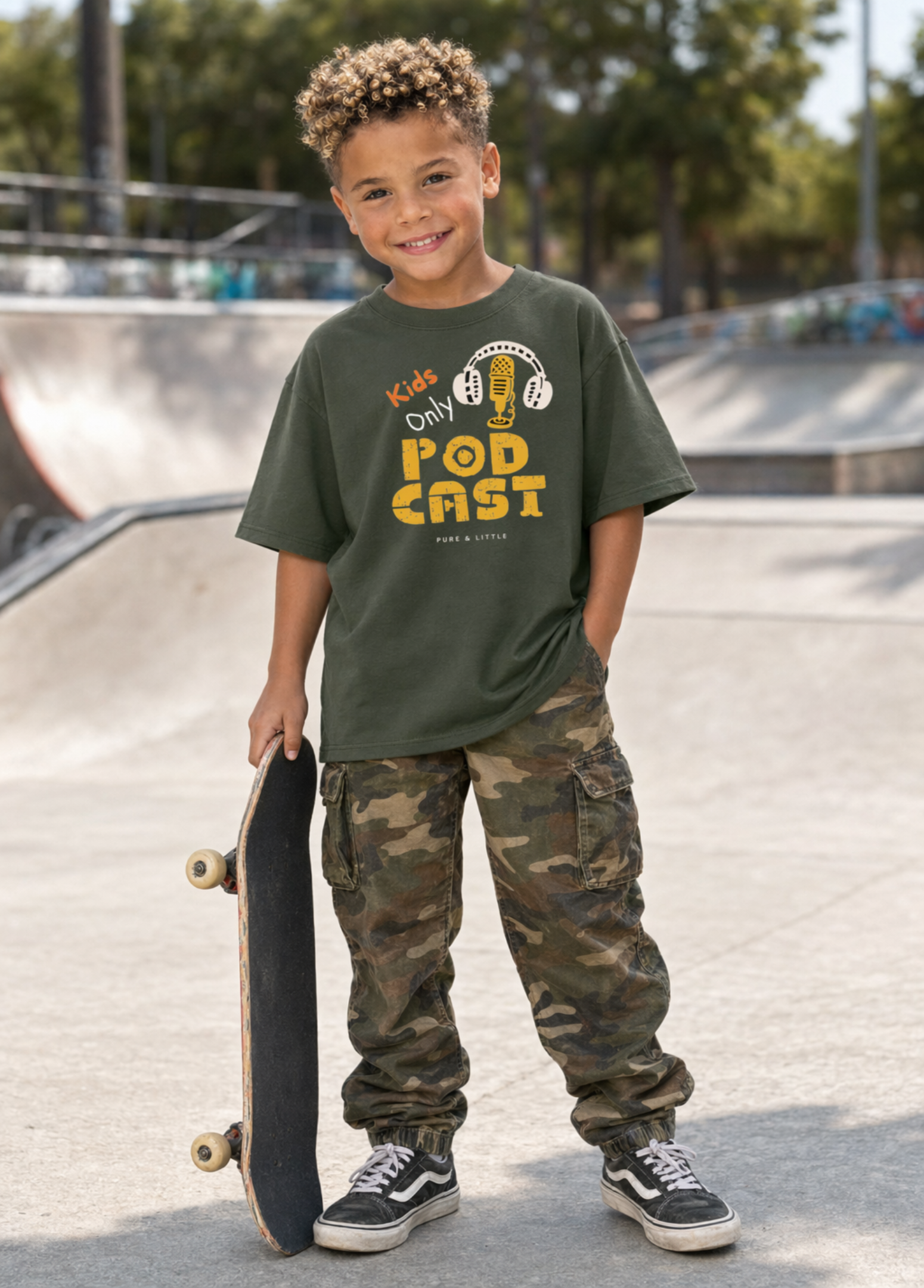 Child wearing a green t-shirt with text and camouflage pants standing at a skate park.