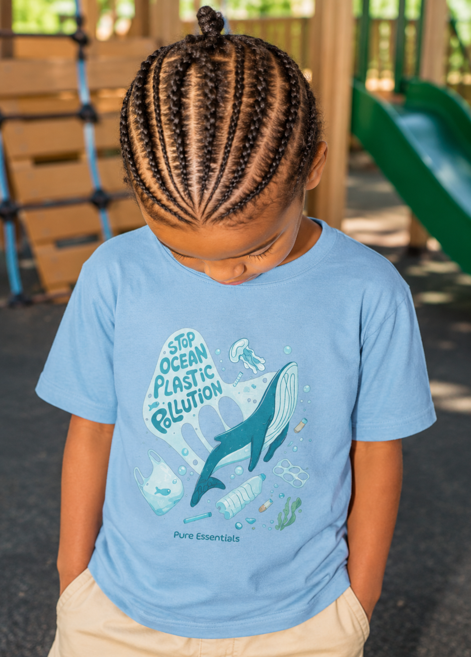 A child wearing a light blue t-shirt with a whale graphic and the text 'STEP OCEAN PLASTIC BILLUTION' by Pure Essentials, standing on a playground.