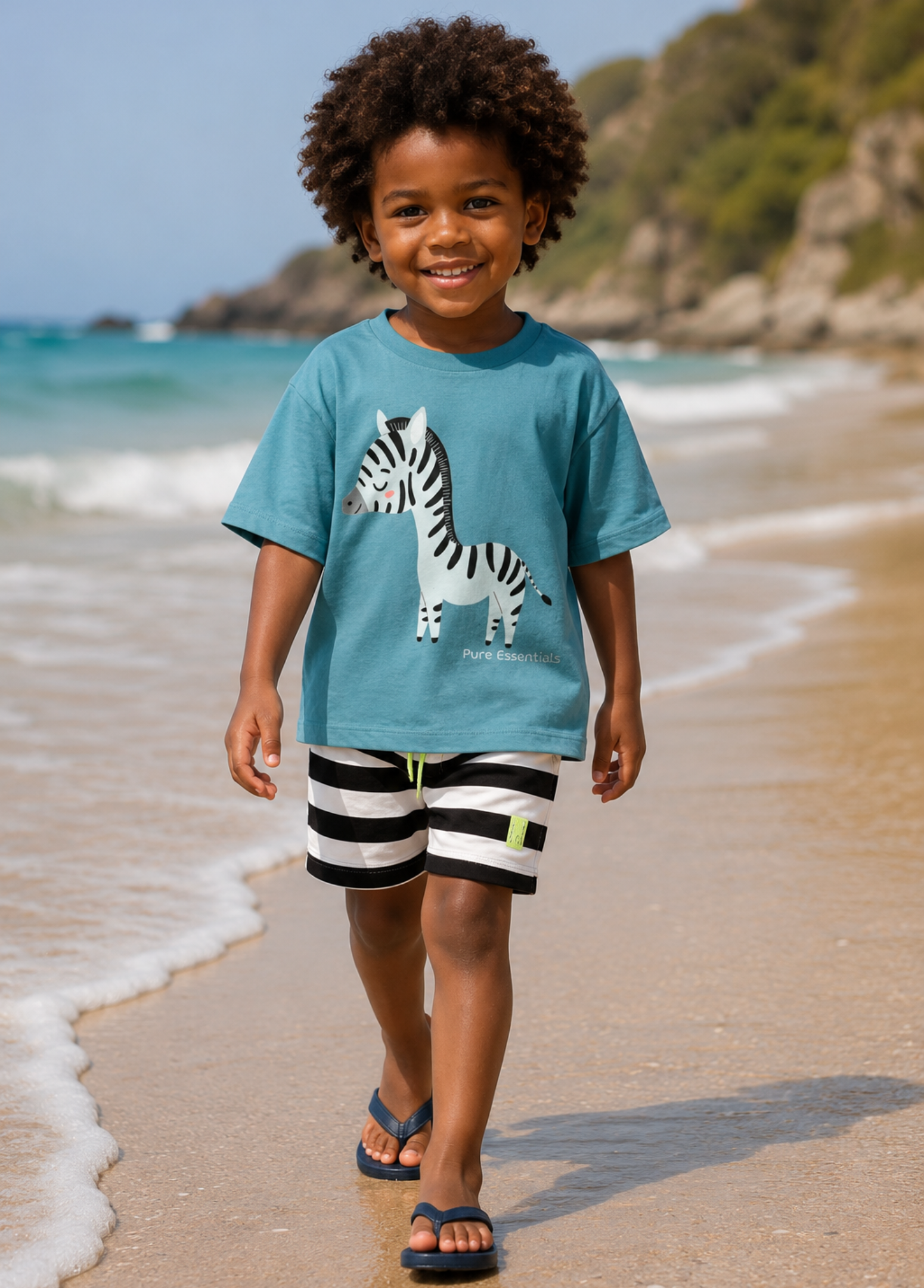 Child wearing a blue t-shirt with a zebra design and black and white striped shorts standing on a beach.