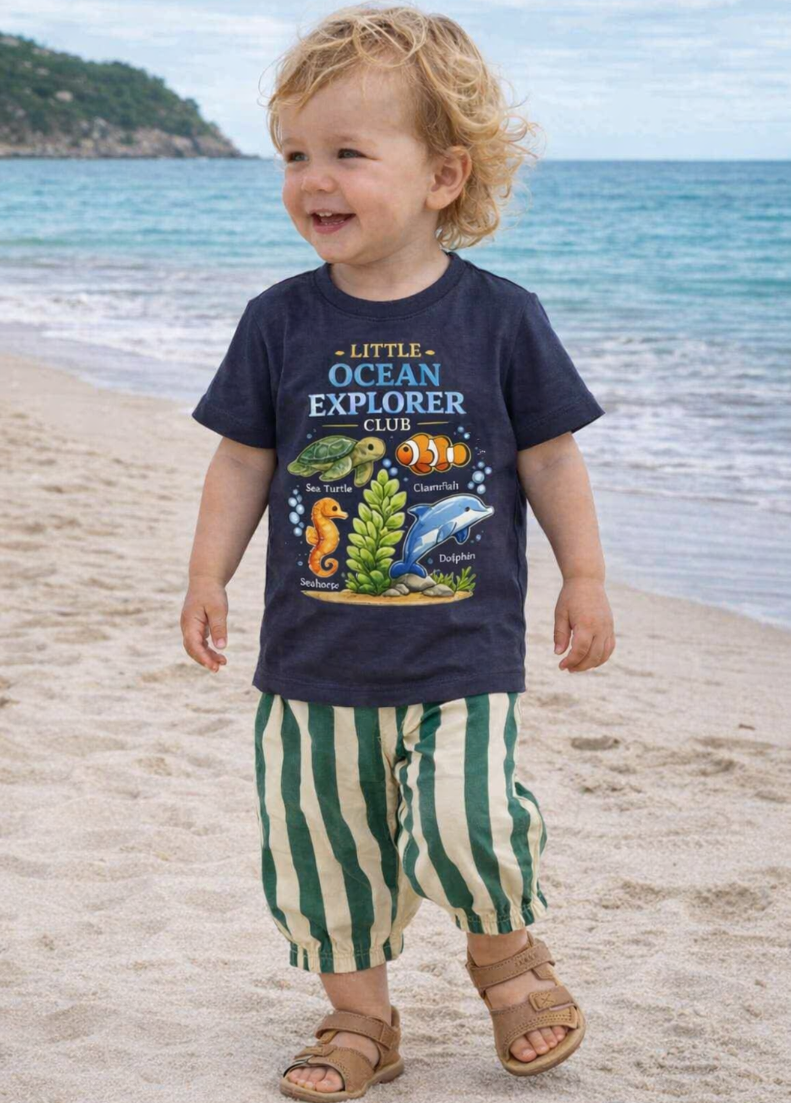 Child wearing a 'Little Ocean Explorer' shirt on a beach